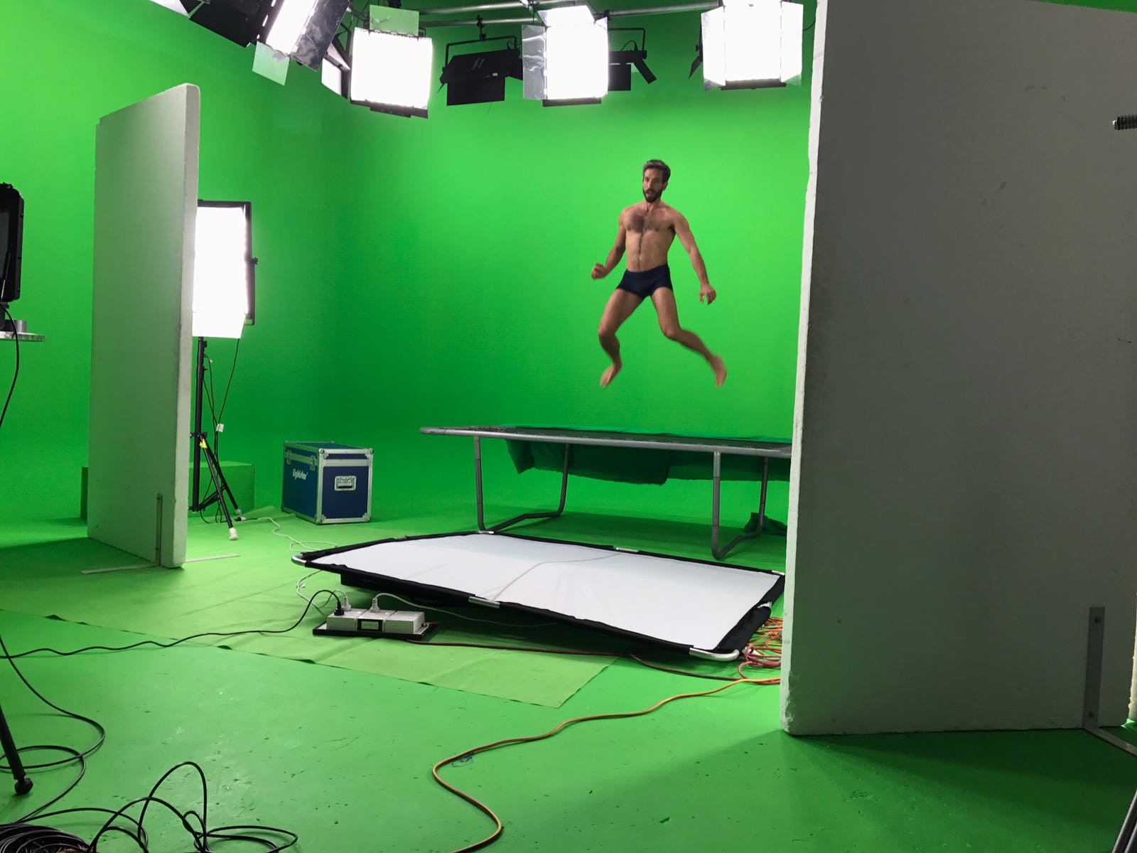 A male model jumping on a trampoline in a green screen studio.