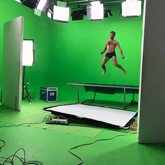 A male model jumping on a trampoline in a green-screen studio.